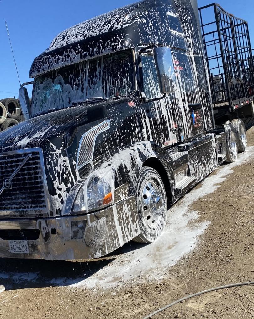 Black Volvo semi truck covered in foam during a wash